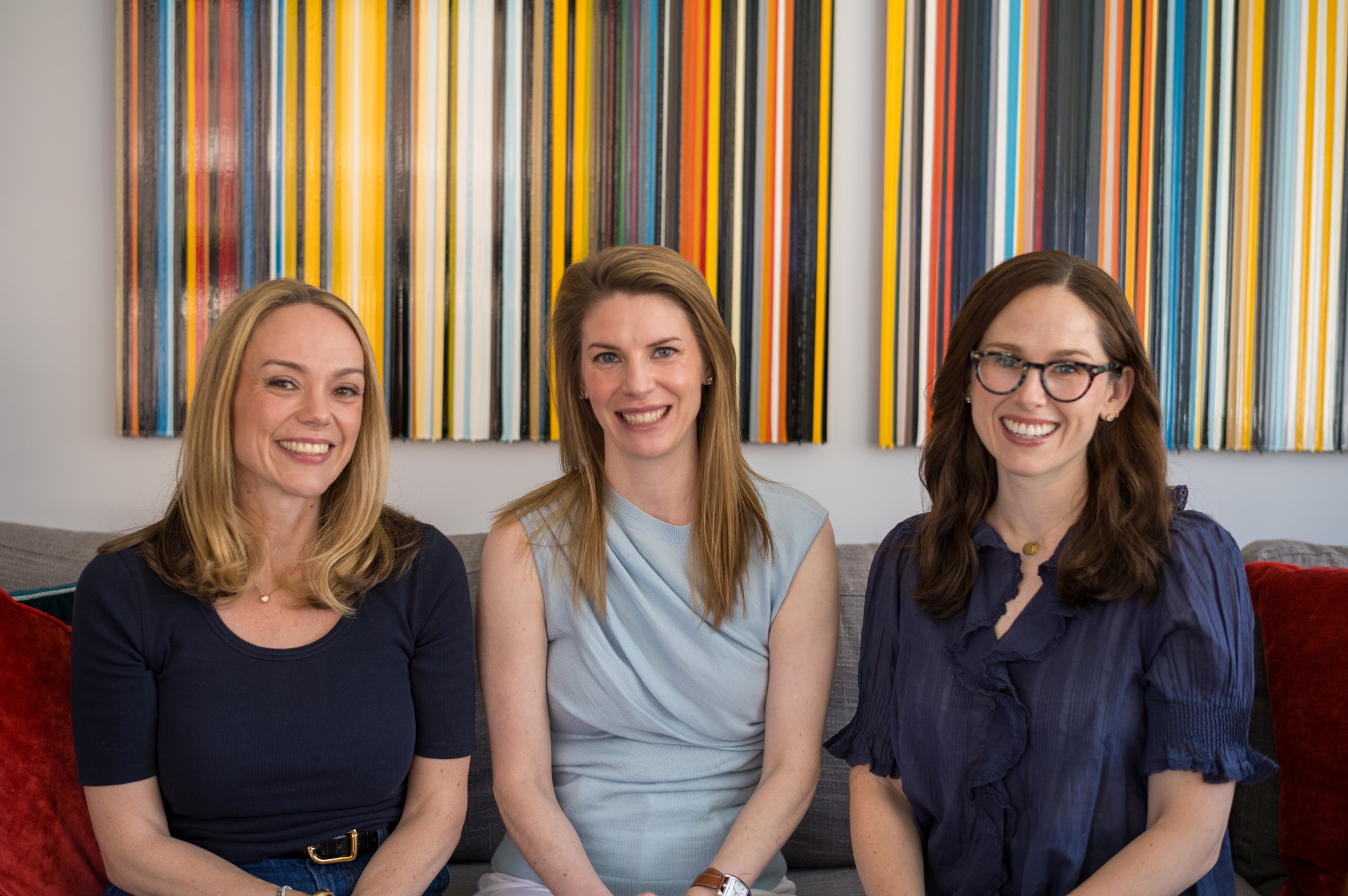 Allie, Katie, and Catey together on a couch beneath two striped paintings